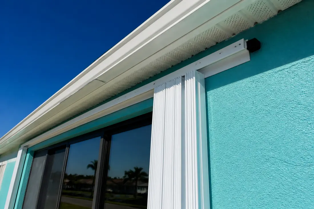 A hurricane shutter track being anchored to a brightly painted stucco wall
