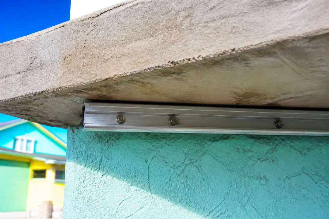 A hurricane shutter track anchored to the underside of a concrete tie beam, fixings in a row along it