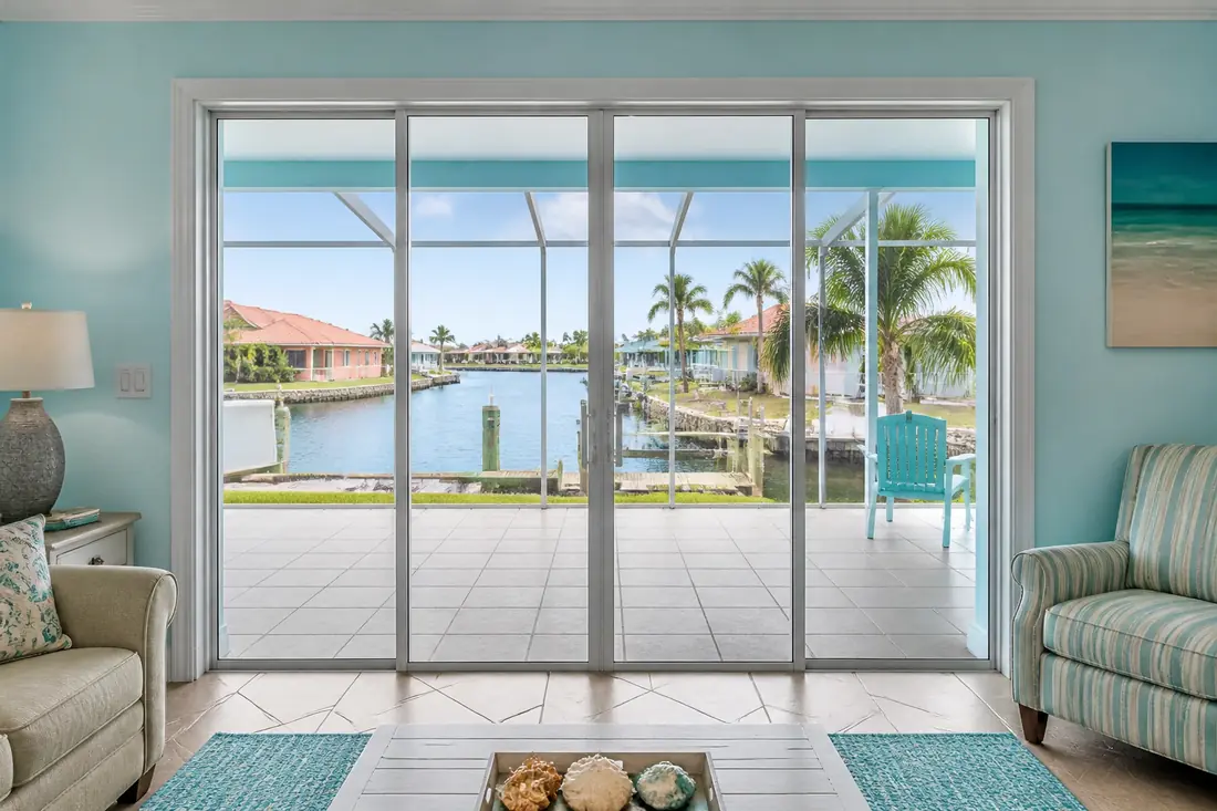 A wide sliding glass door in the rear wall of a house with a lanai floor beyond