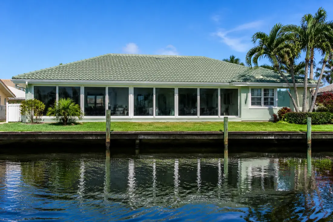 A glazed lanai running across the back of a brightly painted Cape Coral house under an existing tile roof